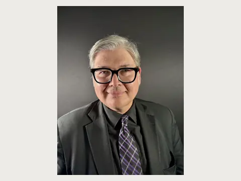 Herbert Midgley in a black suit and glasses against a dark background.