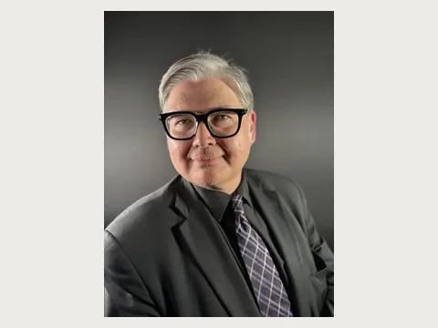 Herbert Midgley in a black suit and glasses against a dark background.