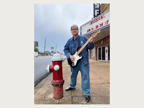 Herbert Midgley holding an electric guitar near a historic theater.