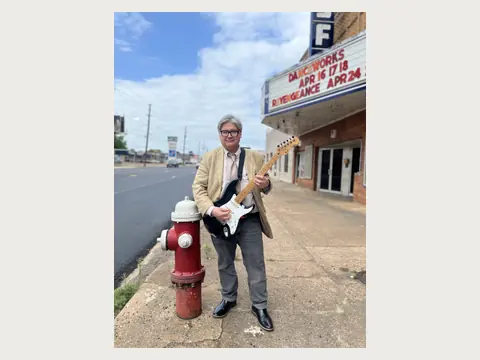 Herbert Midgley holding an electric guitar in downtown East Texas.