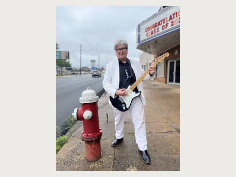 Herbert Midgley playing electric guitar near a historic theater.