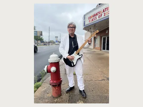 Herbert Midgley playing electric guitar in a white suit.