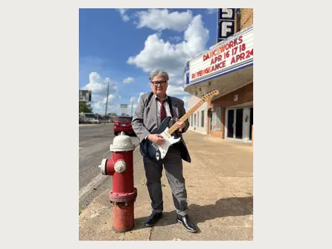 Herbert Midgley holding an electric guitar in a dark suit.