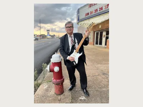 Herbert Midgley holding an electric guitar near a historic theater.