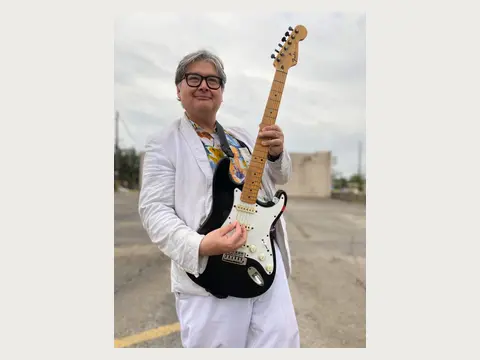 Herbert Midgley holding an electric guitar in a white suit.