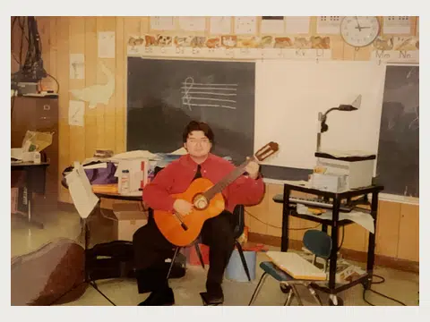 A younger Herbert Midgley teaching guitar in a classroom.